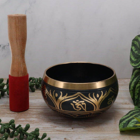 Decorative singing bowl with gold patterns on a wooden surface with a white background