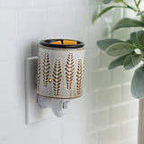 Wall-mounted ceramic wax warmer with leaf pattern on a light tiled wall.