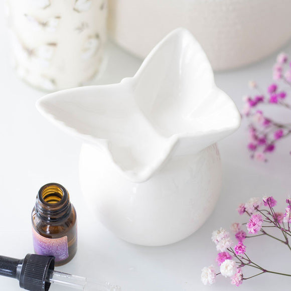 White ceramic diffuser with a bottle of essential oil and pink flowers on a light surface