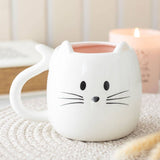 White cat-shaped mug with a pink interior on a textured surface.