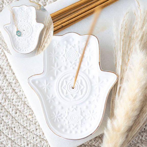 White ceramic incense burner with wooden sticks on a textured surface