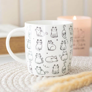 White mug with black cat illustrations on a textured surface with a candle in the background