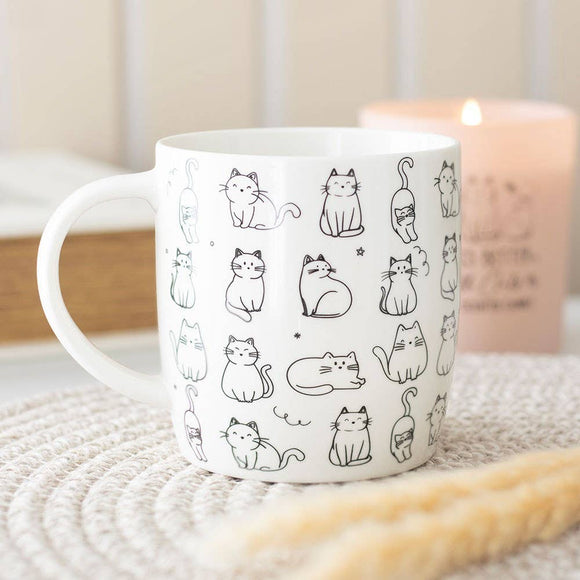 White mug with black cat illustrations on a textured surface with a candle in the background