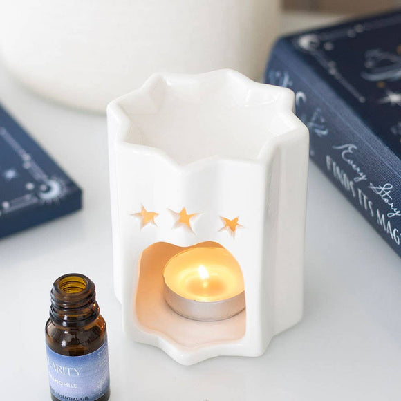 Small white ceramic lamp with a lit candle inside, next to a bottle of Natura Viva essential oil.