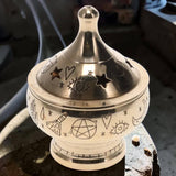 Decorative white and silver incense burner with symbols on a surface