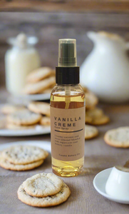 Vanilla creme body spray bottle on a table with cookies and a teapot in the background