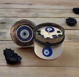 Candle with evil eye design in a metal container on a wooden surface