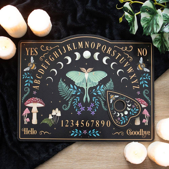 Decorative Ouija board with mystical design on a dark surface with candles and plants.