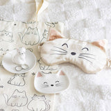 Cat-themed eye mask and small dishes on a white surface with cat illustrations.