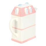 Teapot shaped like a house with pink roof and trim on a white background