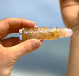 Hand holding a 'Crystal Healing' rollerball with a blurred blue background