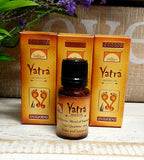 A bottle of Yatra Aroma Oil with its packaging boxes in the background, placed on a wooden surface with a purple flower in the background.